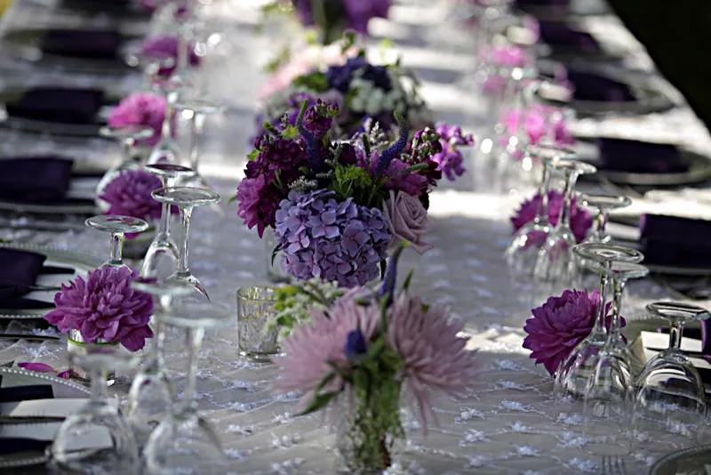 Une longue table fleurie de dahlias et d’hortensias violets, serviettes aubergine