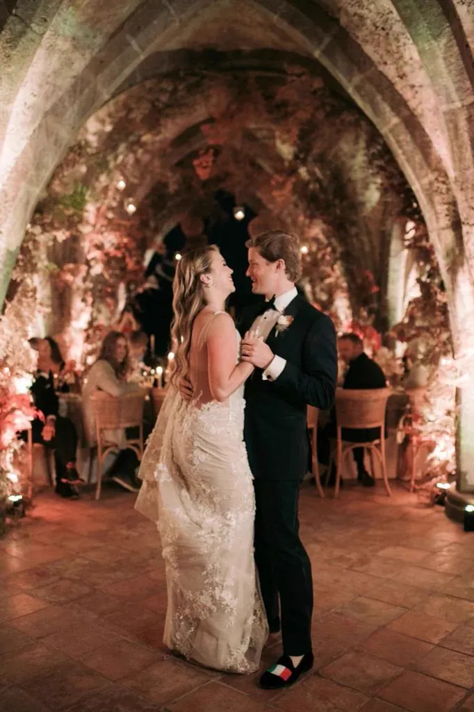 Les mariés ouvrent le bal sous une voûte de pierre fleurie, dans une lumière chaude, les invités assis autour