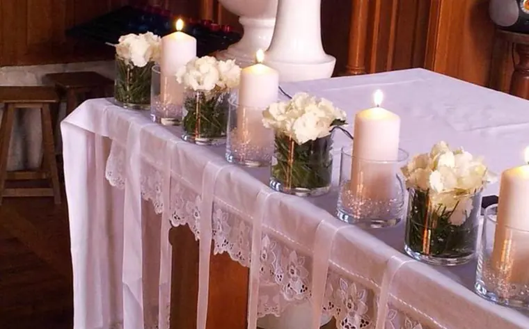 Le détail de la table d’autel : organza, dentelle, bougies et petits bouquets de roses blanches