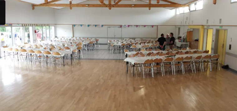 La salle nue, avant : chaises pliantes, tables en enfilade et fanions de la commune