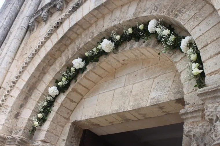guirlande de roses blanches et de gypsophile courant sur le fronton en pierre de l eglise