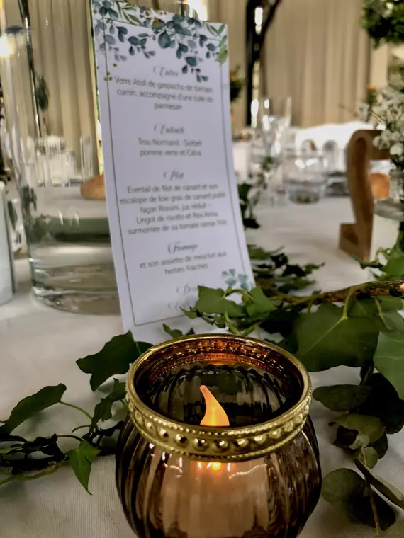 Le menu et un photophore doré, sur une table dressée sous la verrière