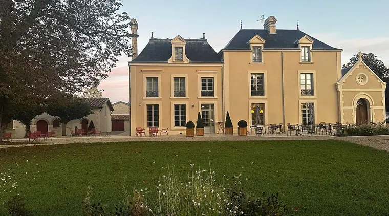 La façade de la demeure au crépuscule, la chapelle accolée sur la droite, et la pelouse devant