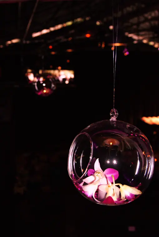 Une boule de verre suspendue à un fil, avec une orchidée et une bougie à l’intérieur