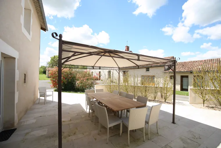 La cour des Gîtes de la Font, ses bâtiments en pierre et sa grande table sous la pergola