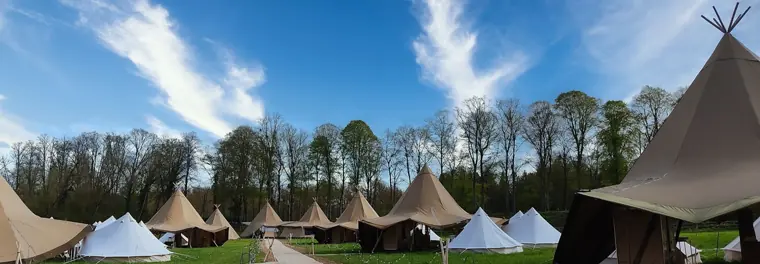 Un champ de tipis et de tentes toilées alignés dans un parc, un chemin de gravier entre eux