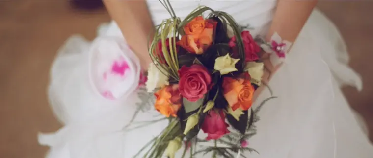 Le bouquet de la mariée, roses orange et corail, tenu contre sa robe