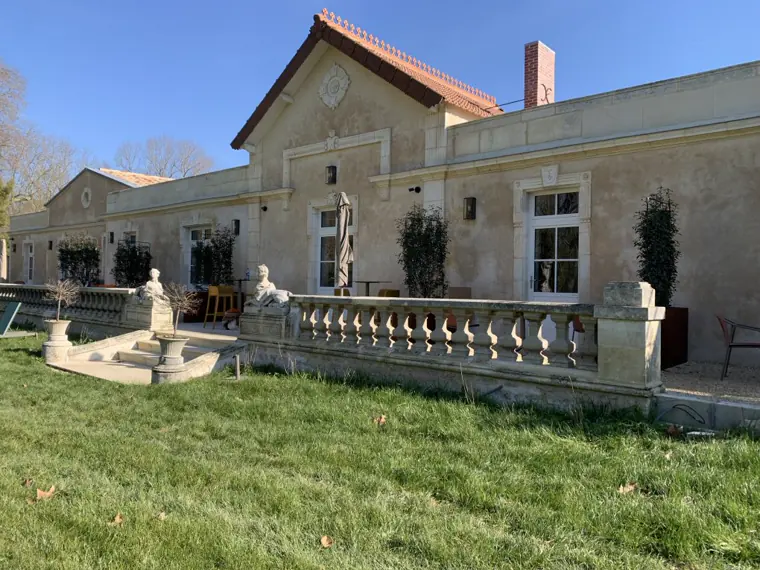 La façade en pierre du Logis de l’Héronière et sa terrasse bordée d’une balustrade, ouverte sur la pelouse