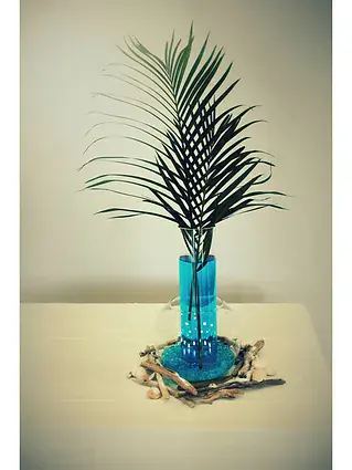 petit vase turquoise surmonte d une palme, pose sur une nappe blanche