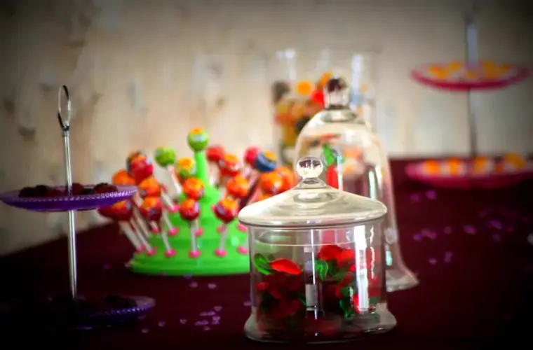 Le bar à bonbons, cloches de verre et présentoirs colorés sur nappe prune