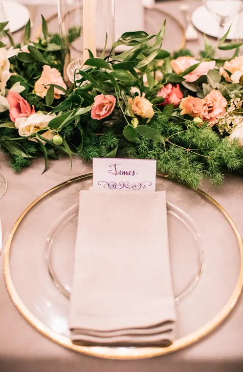 un marque-place manuscrit posé sur la serviette rose poudré et l’assiette cerclée d’or