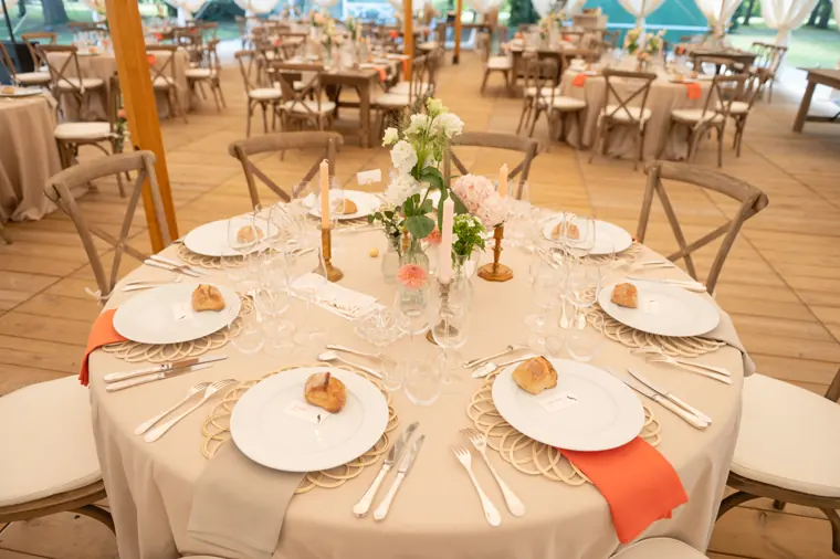 Table ronde dressée : serviettes corail, sets en rotin et fleurs dans les tons pêche