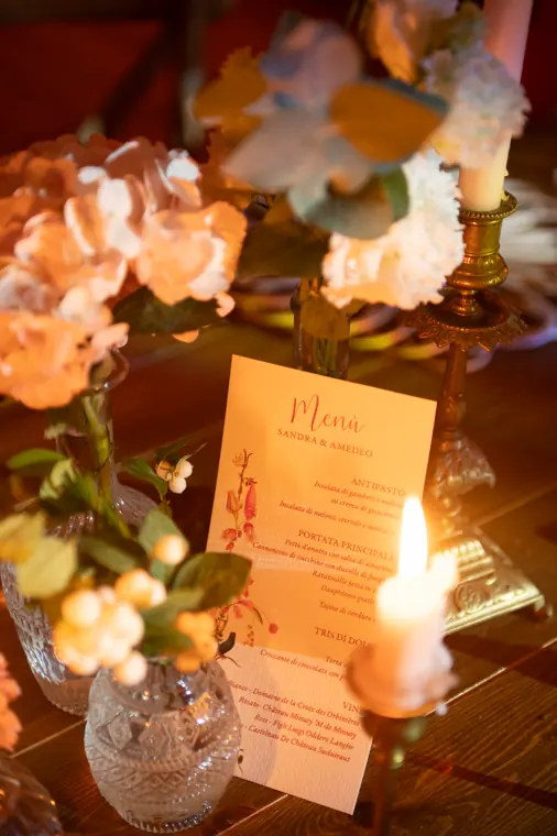 Détail d’une table le soir : le menu, les bougies et les fleurs