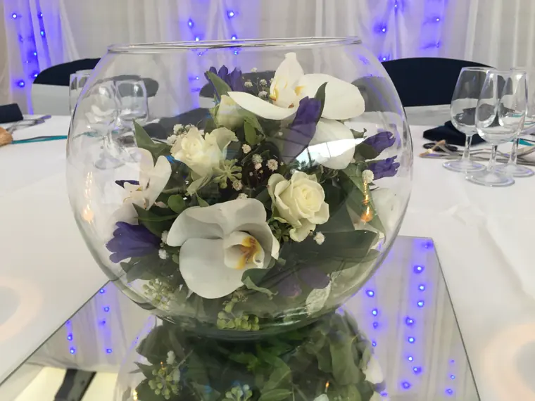 Une boule de verre posée sur miroir, orchidées blanches et roses immergées