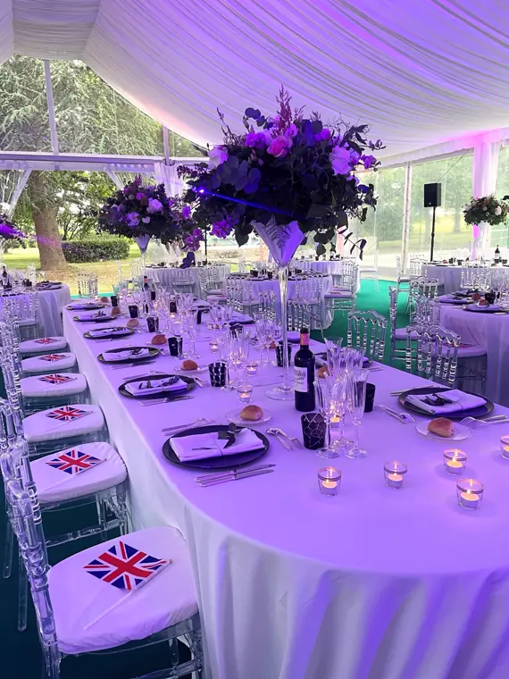 Grande table de mariage. Nappe blanche et photophores allumés. Drapeaux anglais sur les chaises