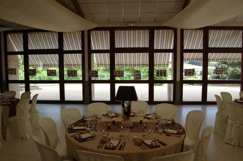 la salle du domaine, tables rondes dressees devant les grandes baies vitrees ouvertes sur le parc