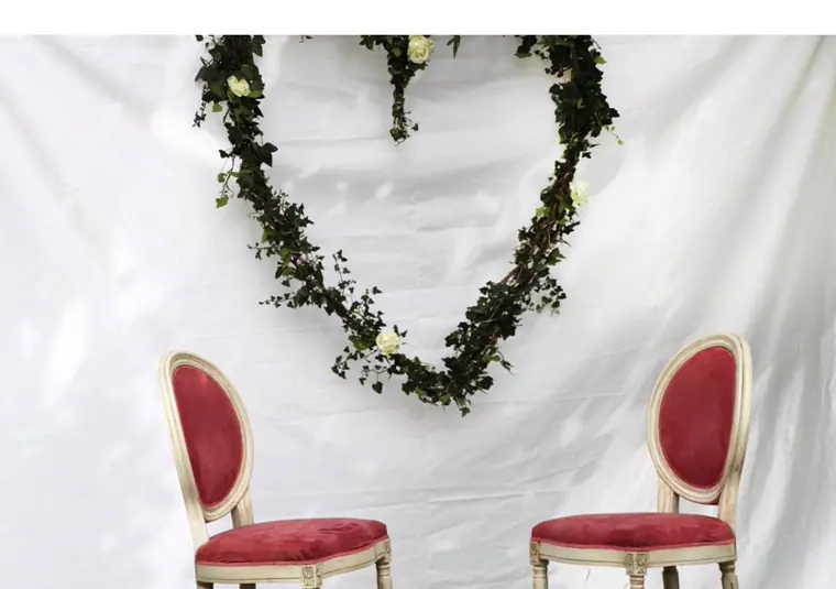 Un cœur de lierre et de roses blanches accroché à la toile, devant deux chaises rouges