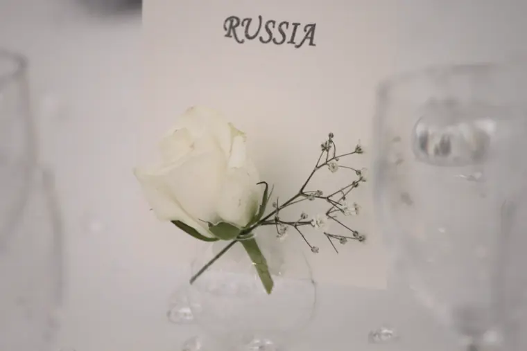 Un marque-place : une rose blanche, un brin de gypsophile, et un nom de pays