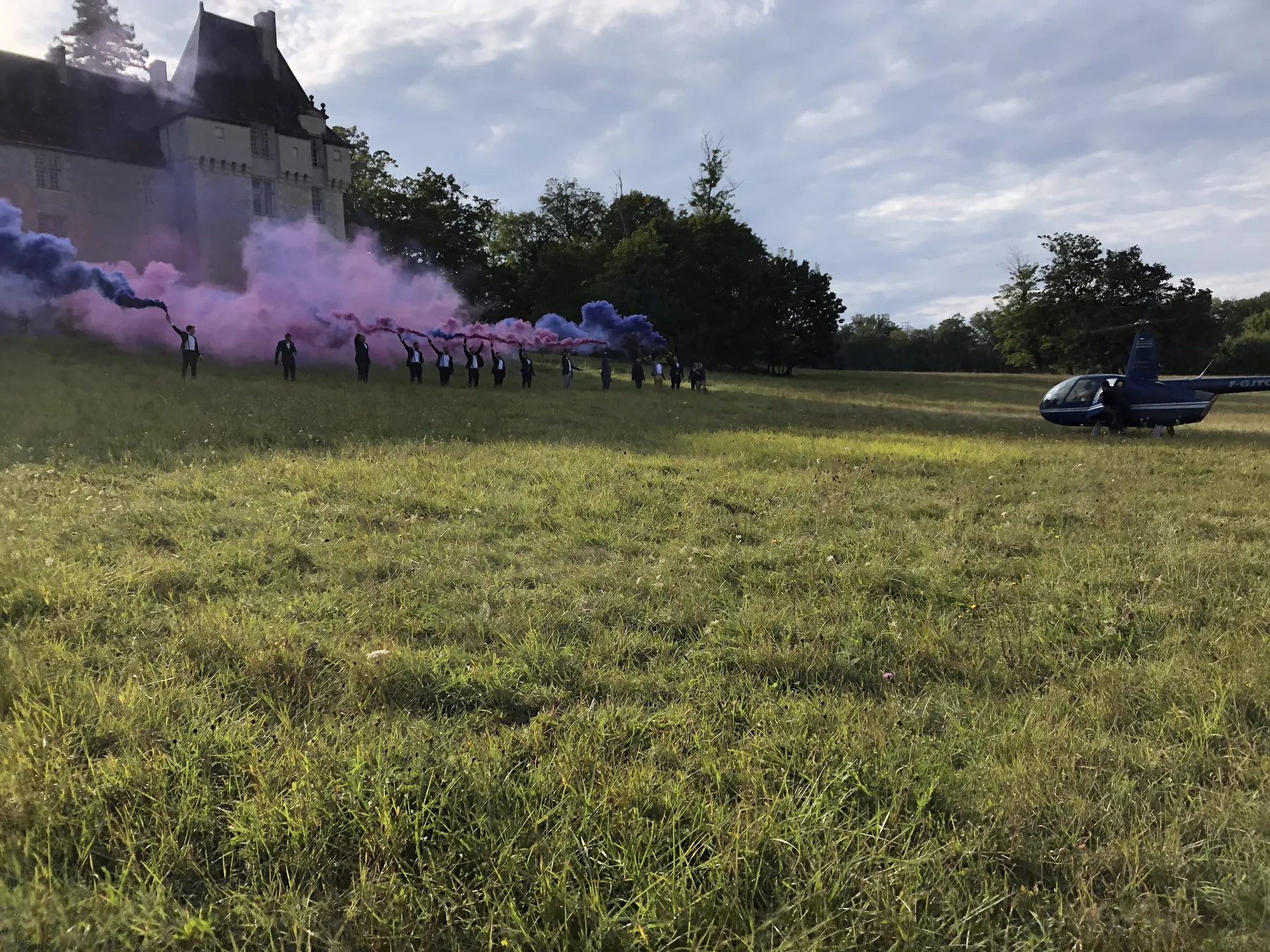 Les invit&eacute;s mass&eacute;s dans le champ, dans la fum&eacute;e rose, attendant l&rsquo;arriv&eacute;e des mari&eacute;s