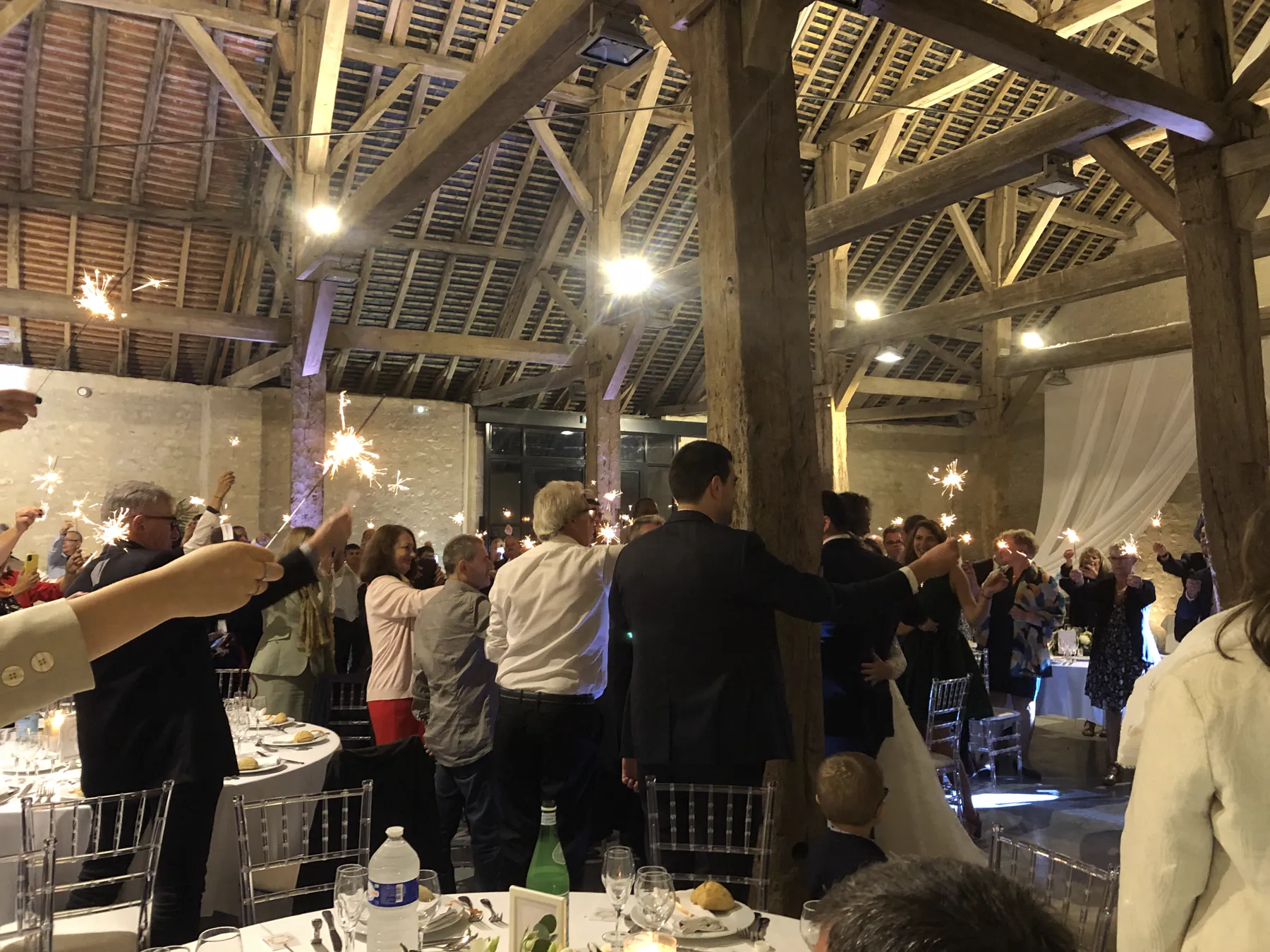 Les invités rassemblés sous la grange en soirée, cierges magiques allumés