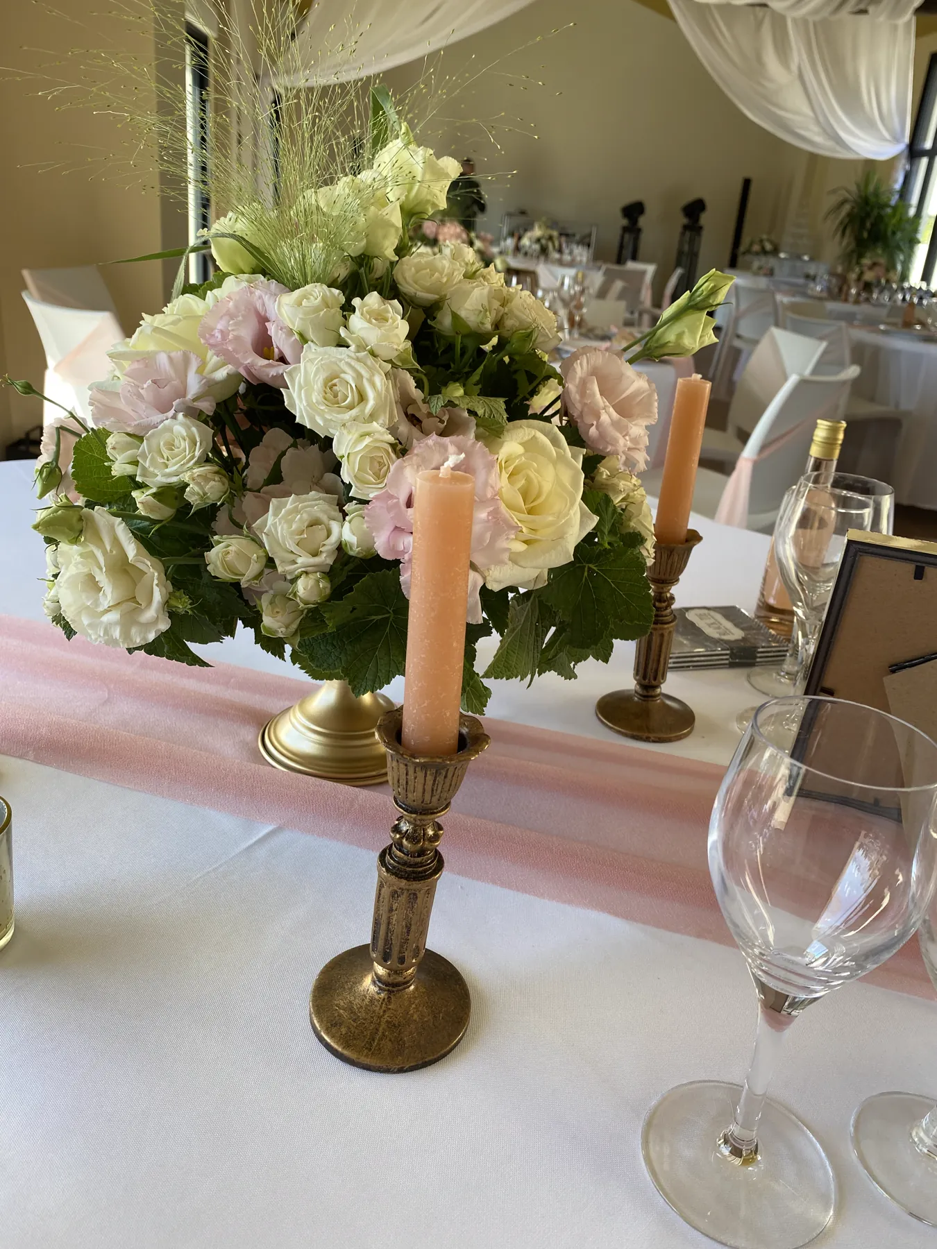 Bougeoirs dorés et bougies crème au milieu des roses, sur la table dressée