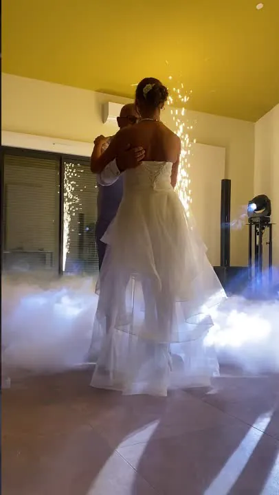 Les mari&eacute;s enlac&eacute;s pour leur premi&egrave;re danse, devant une fontaine d&rsquo;&eacute;tincelles et dans la fum&eacute;e lourde