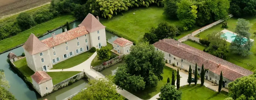 Vue aérienne du domaine : le château et ses douves à gauche, les anciens bâtiments agricoles et la piscine à droite