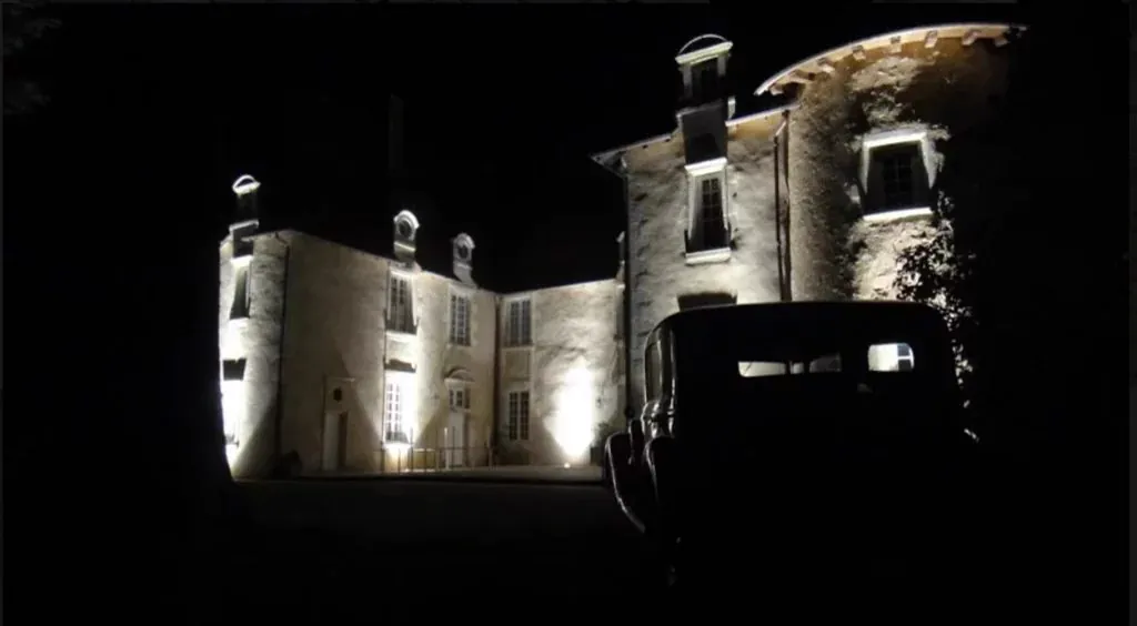 La façade du château éclairée dans la nuit, une voiture ancienne garée devant