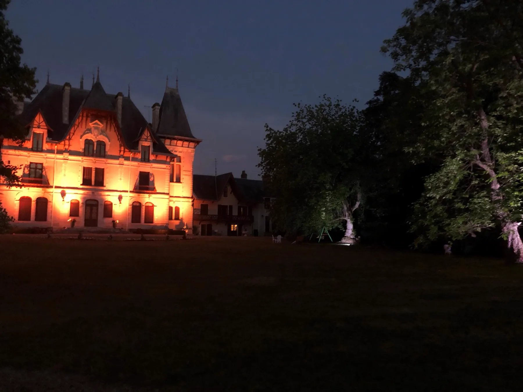 La façade du château illuminée à la nuit tombée, vue depuis le parc