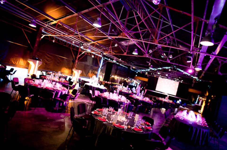 La halle de l&rsquo;ancienne carrière dressée en tables rondes, sous la charpente métallique et les lumières violettes