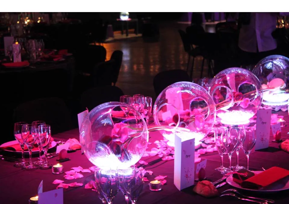La table éclairée de rose, boules de verre lumineuses et pétales sur la nappe sombre