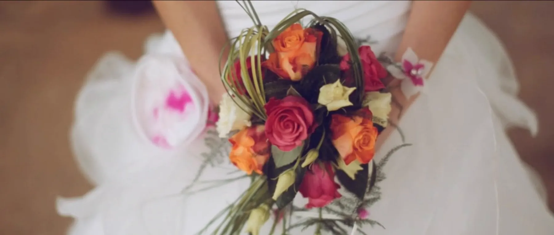 La mari&eacute;e tient son bouquet orange et corail contre sa robe