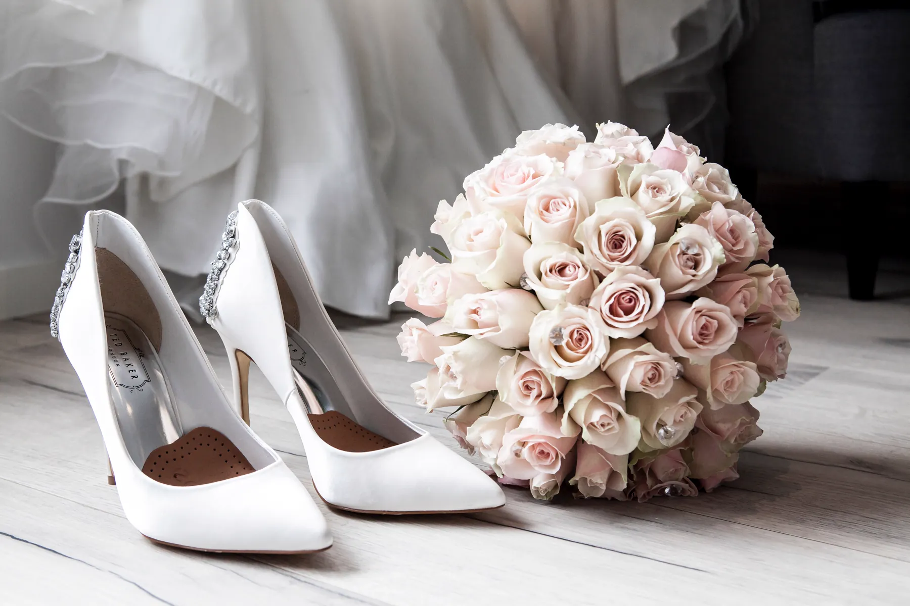 Les escarpins blancs et le bouquet de roses posés sur le parquet, devant la robe