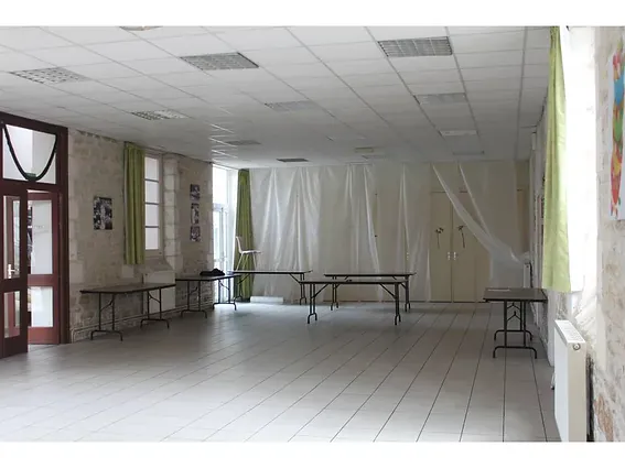 La cantine de l’école vide : sol clair, faux plafond &agrave; dalles, tables pliantes et placards le long du mur