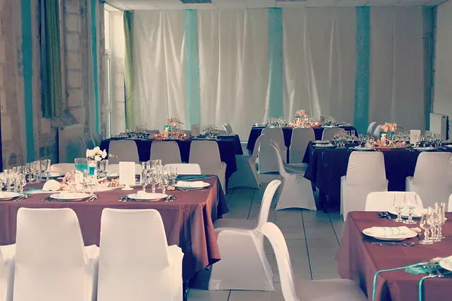 La salle habill&eacute;e de voilages turquoise et blancs, longues tables en chocolat et housses blanches