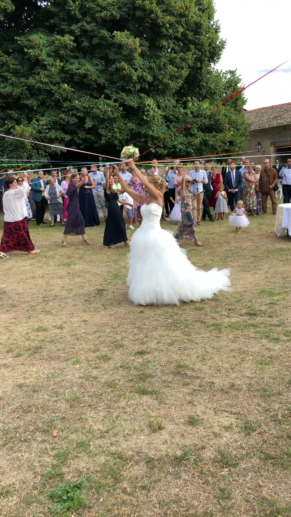 La mariée tient le bouquet, les rubans tendus vers les invitées