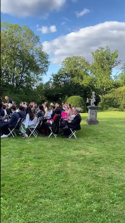 Les invit&eacute;s assis en rangs sur la pelouse du parc, devant une statue, pendant la c&eacute;r&eacute;monie