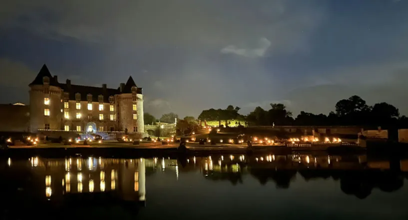 Le château de la Roche Courbon illuminé la nuit, les jardins jalonnés de lumières et leur reflet dans la pièce d’eau