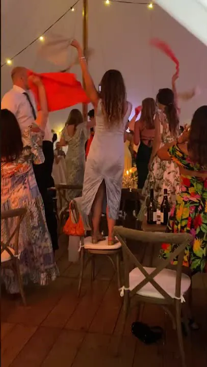 Les invit&eacute;s debout sur les chaises agitent leurs serviettes corail au-dessus de leur t&ecirc;te