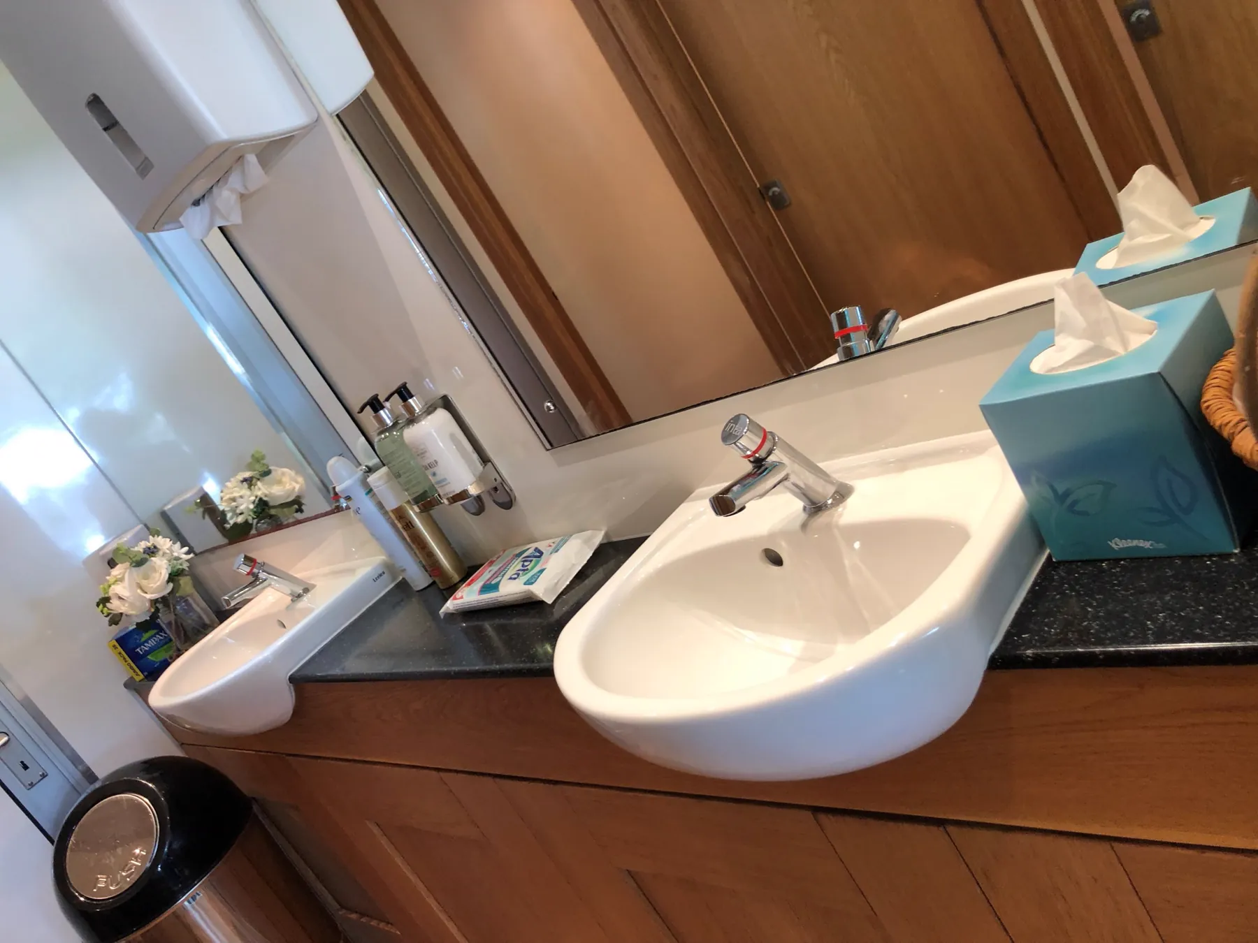 L’intérieur d’un sanitaire mobile : deux lavabos en porcelaine, plan de granit, miroir, savon et fleurs