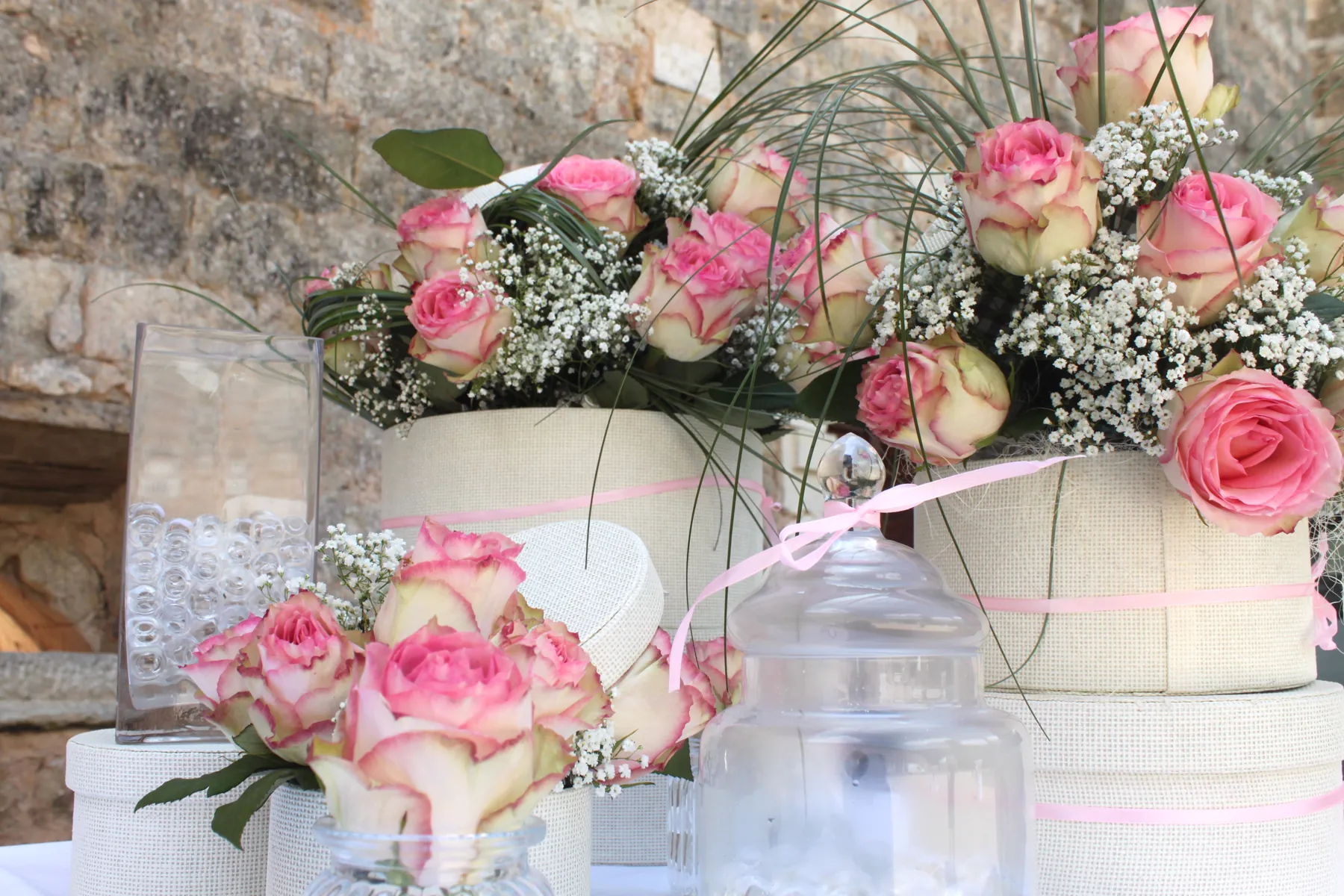 Des roses blanches et roses dress&eacute;es dans des bo&icirc;tes &agrave; chapeau, devant le mur de pierre de l&rsquo;abbaye